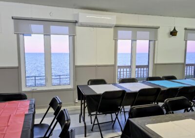 Salle du 1740 aménagée avec tables, chaises, fenêtres avec vue sur le lac et équipement de son à Mashteuiatsh.